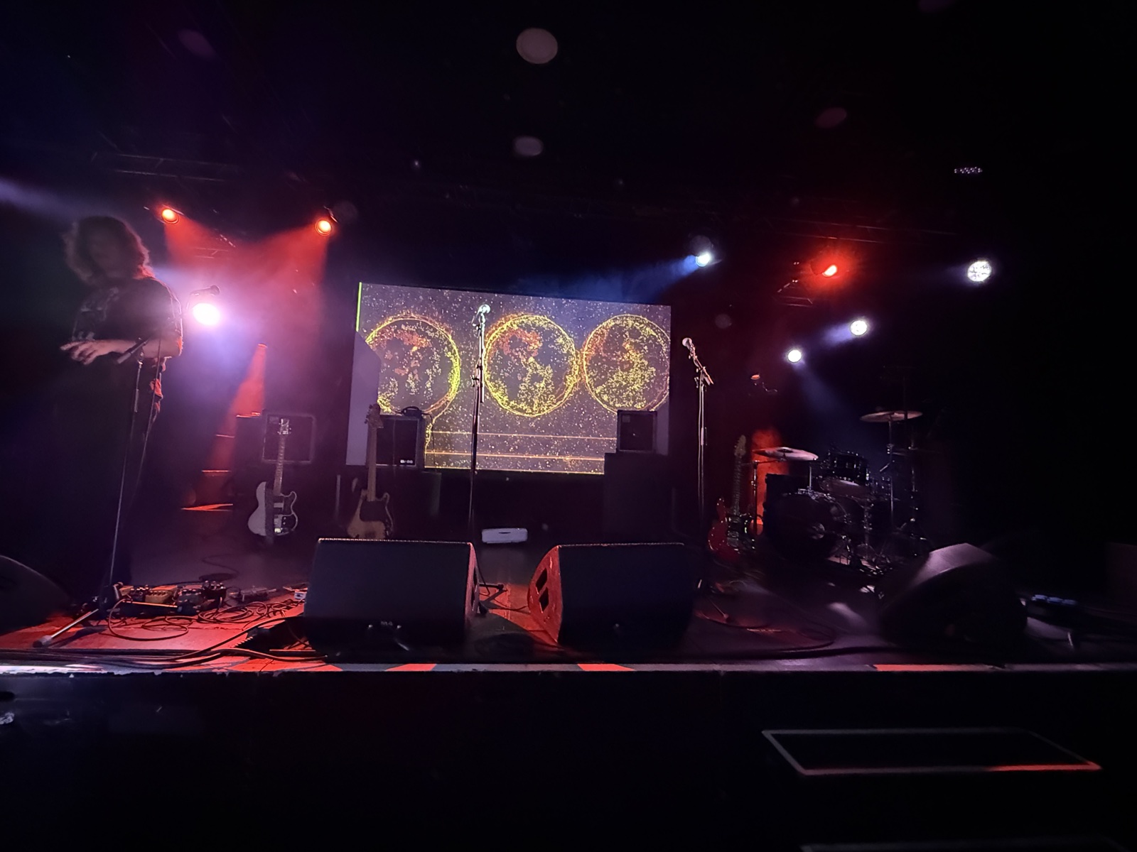 Empty Tolhuistuin stage at soundcheck, with a petri-dish image projected on the back screen and gear scattered across the floor.