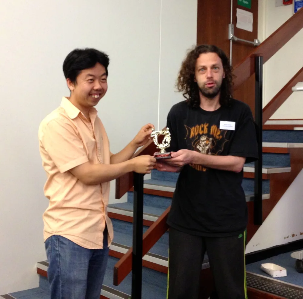 Two researchers on a staircase at a workshop, handing over a small gold trophy: YY Ahn on the left takes it from Mason Porter on the right